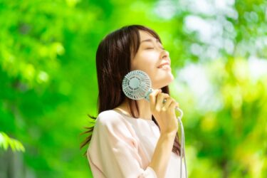 顔に冷却プレート付きハンディファンを付けている女性