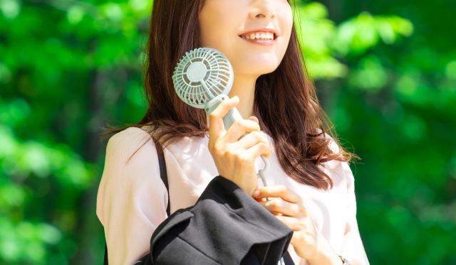 顔に冷却プレート付きハンディファンを付けている外出中の女性