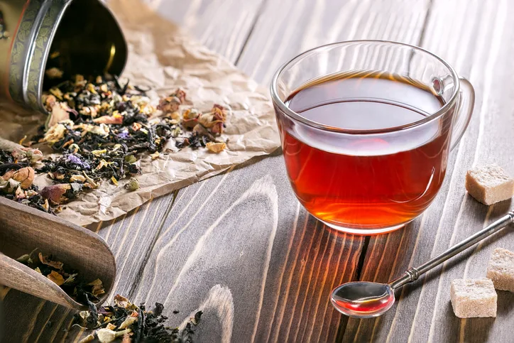 紙に散らばった花茶葉とハーブティー&透明なカップ